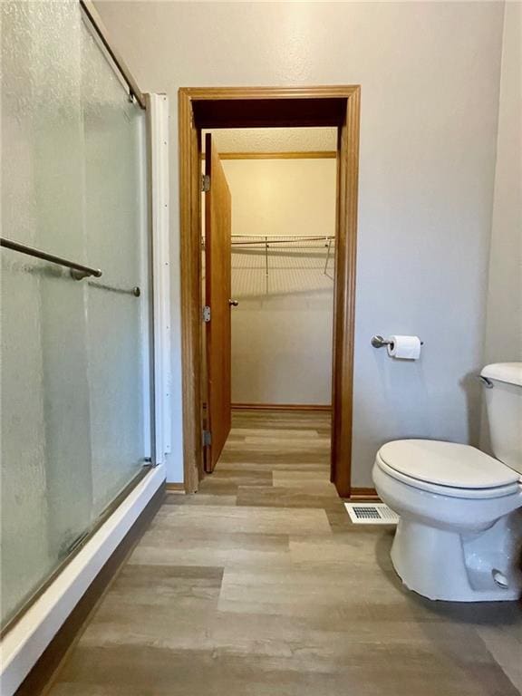 bathroom with wood-type flooring, a shower with shower door, and toilet