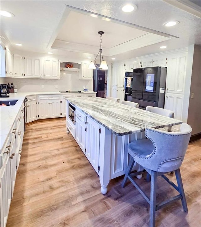 kitchen featuring light wood-type flooring, white cabinetry, black appliances, and a raised ceiling