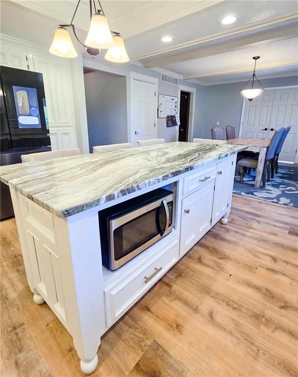 kitchen featuring stainless steel microwave, beamed ceiling, light wood-type flooring, light stone counters, and white cabinets