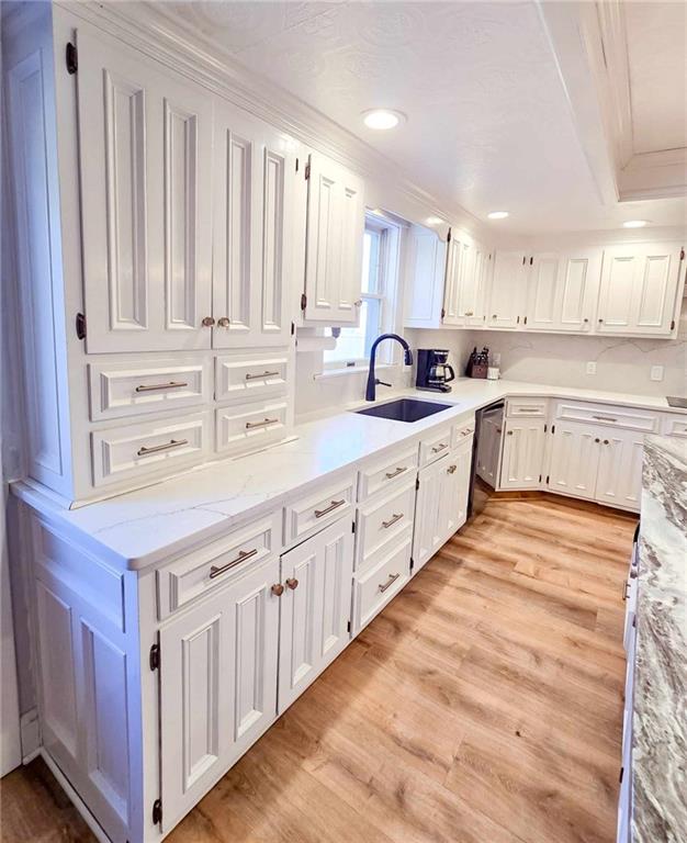 kitchen with light stone countertops, dishwasher, light wood-style flooring, white cabinetry, and a sink