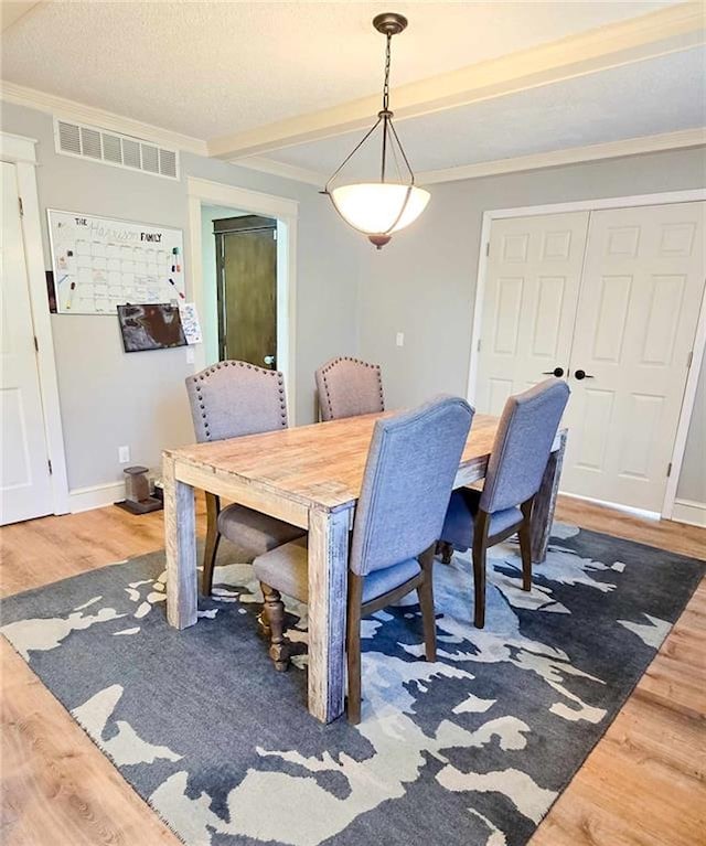 dining room with baseboards, wood finished floors, visible vents, and ornamental molding