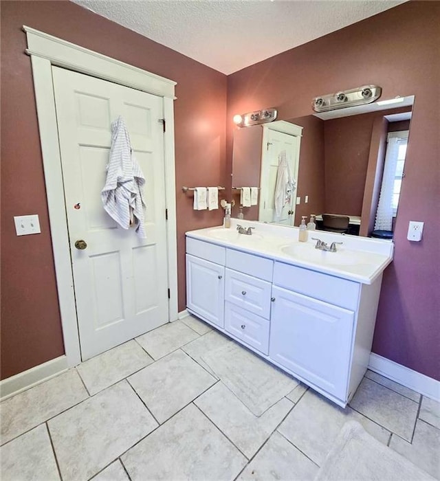 full bathroom featuring a sink, a textured ceiling, baseboards, and double vanity