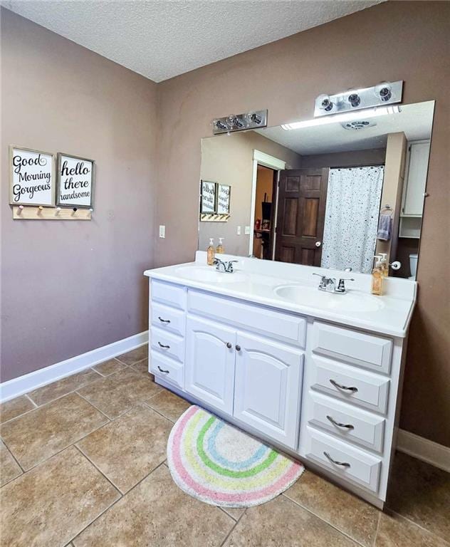 full bath with double vanity, a textured ceiling, baseboards, and a sink