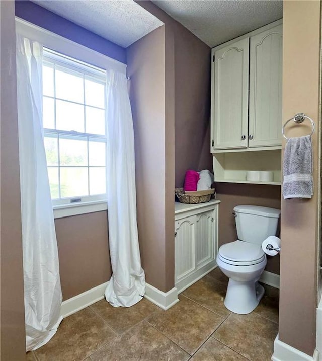 bathroom featuring baseboards, toilet, tile patterned flooring, and a textured ceiling