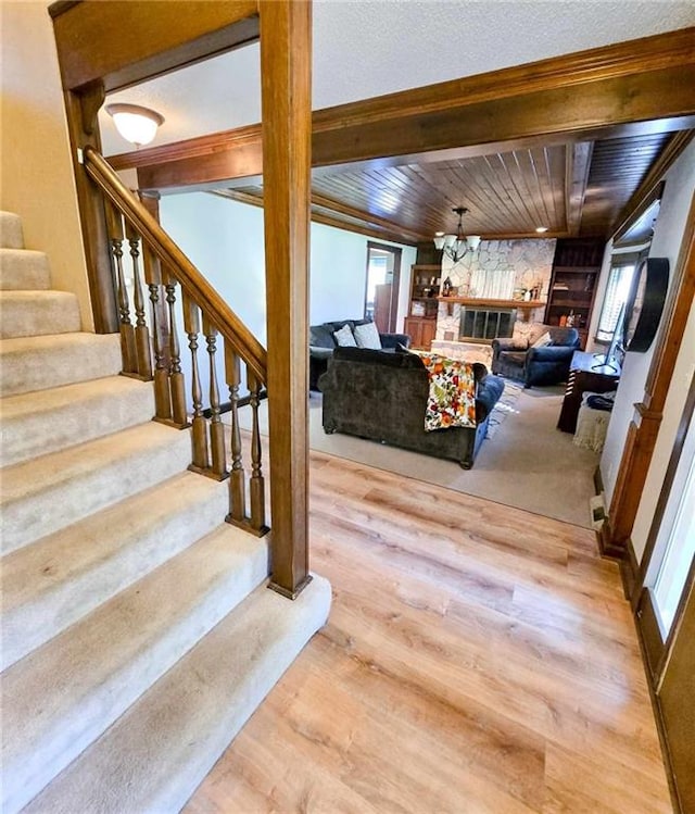 stairs with wood finished floors, beam ceiling, wooden ceiling, and a fireplace