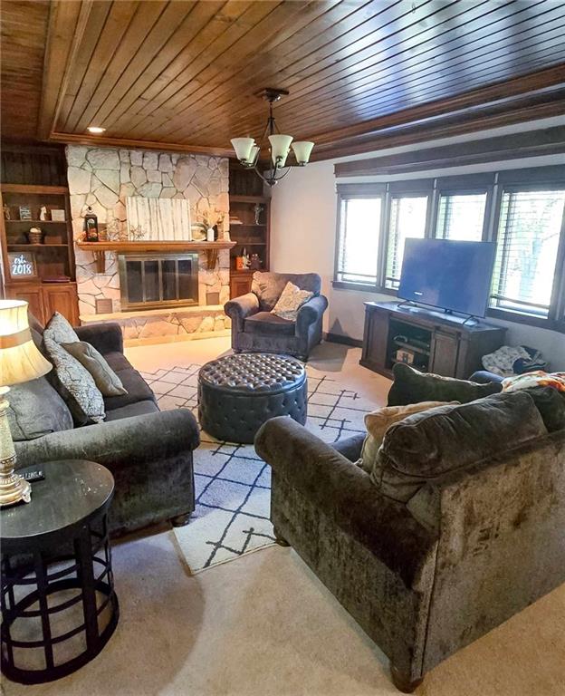 carpeted living area featuring a stone fireplace, an inviting chandelier, and wood ceiling