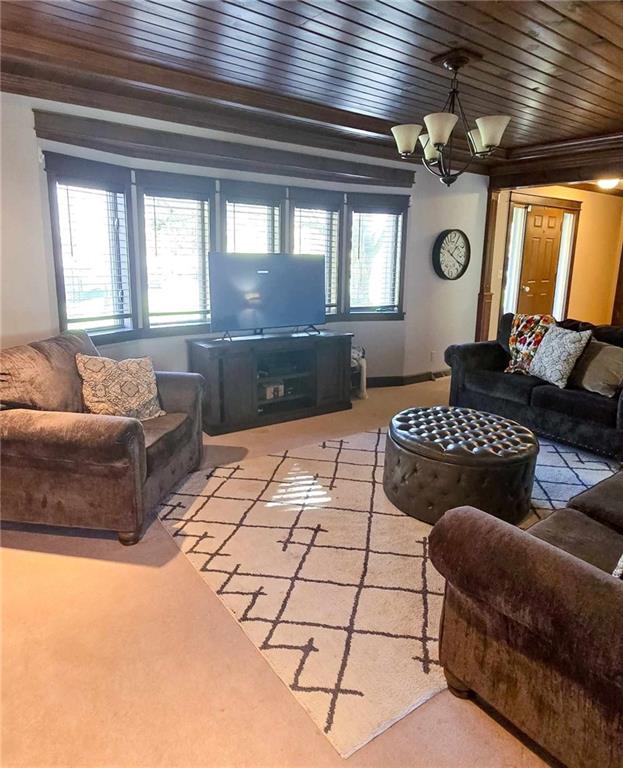 carpeted living area with wood ceiling, a healthy amount of sunlight, and an inviting chandelier