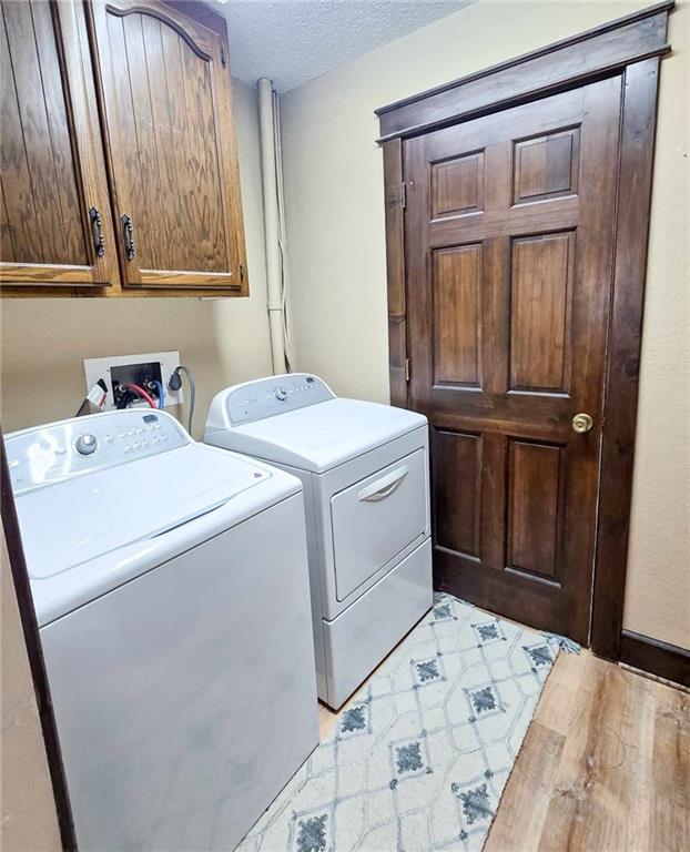 clothes washing area with light wood finished floors, cabinet space, washer and dryer, and a textured ceiling