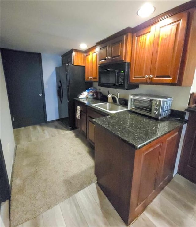 kitchen featuring black appliances, a sink, dark stone countertops, brown cabinetry, and a toaster