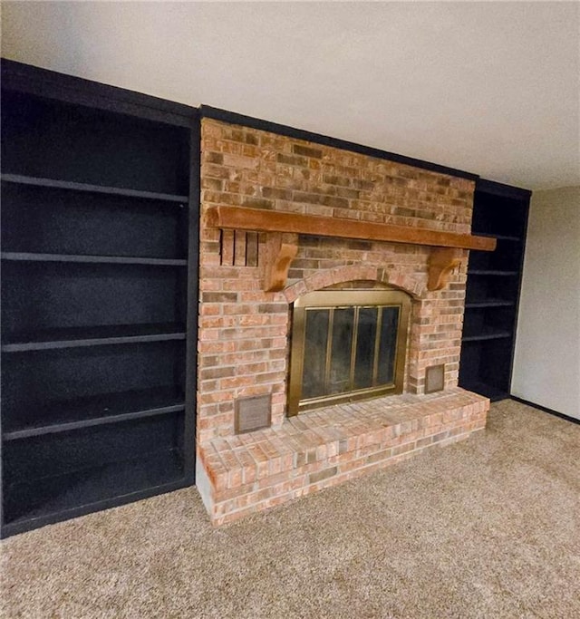 unfurnished living room with a brick fireplace, built in shelves, and carpet floors