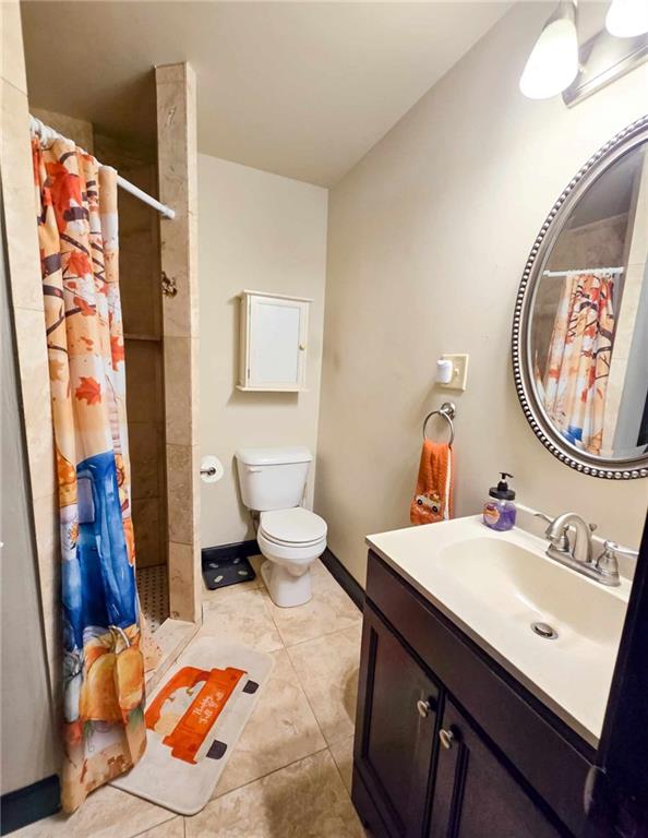 full bathroom with vanity, baseboards, tiled shower, tile patterned floors, and toilet