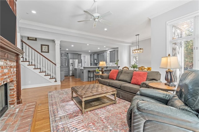 living area featuring a fireplace, stairway, ornamental molding, light wood-type flooring, and baseboards