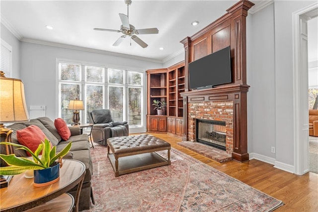 living area featuring a ceiling fan, a fireplace, crown molding, and light wood finished floors