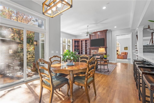 dining area featuring visible vents, stairs, crown molding, a stone fireplace, and light wood-type flooring