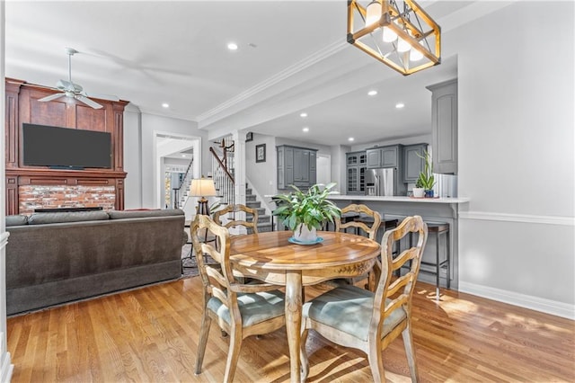 dining room with ceiling fan with notable chandelier, baseboards, stairs, ornamental molding, and light wood finished floors