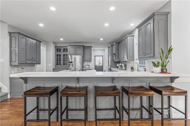 kitchen with a peninsula, high quality fridge, gray cabinets, and wood finished floors