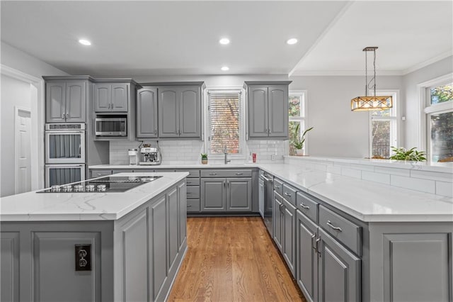 kitchen with tasteful backsplash, appliances with stainless steel finishes, wood finished floors, a peninsula, and gray cabinets