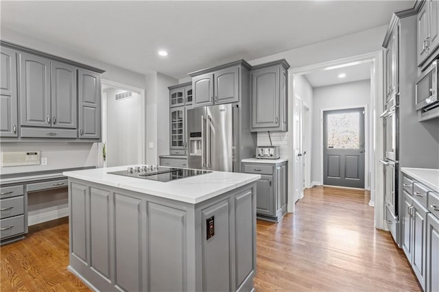 kitchen featuring tasteful backsplash, appliances with stainless steel finishes, a center island, gray cabinets, and light wood-type flooring