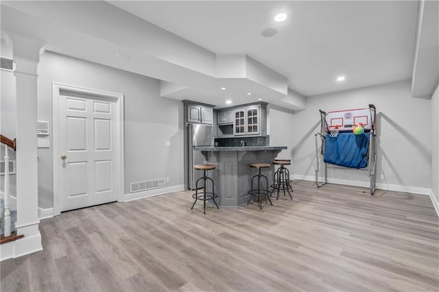 kitchen featuring light wood-style flooring, gray cabinetry, a kitchen breakfast bar, freestanding refrigerator, and glass insert cabinets