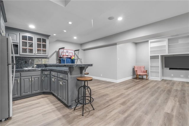 kitchen featuring a breakfast bar area, freestanding refrigerator, a peninsula, gray cabinets, and light wood-style floors