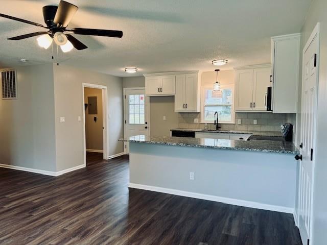 kitchen with black range oven, dark hardwood / wood-style flooring, kitchen peninsula, white cabinets, and dark stone countertops