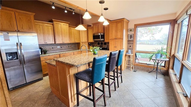 kitchen with light stone counters, a breakfast bar, a kitchen island with sink, stainless steel appliances, and decorative light fixtures