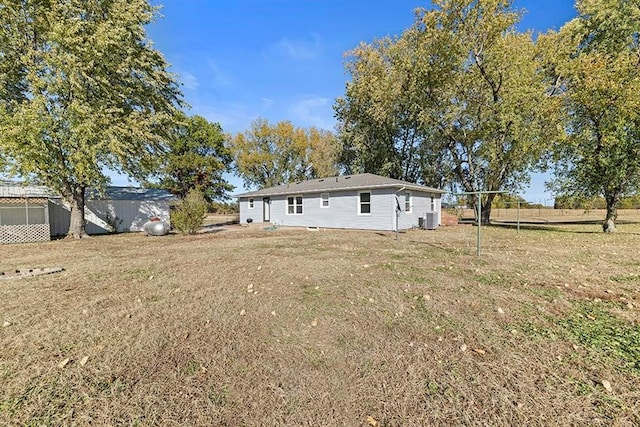 rear view of property featuring central AC unit and a lawn