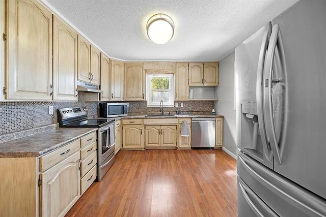 kitchen with light brown cabinets, appliances with stainless steel finishes, a textured ceiling, wood-type flooring, and sink