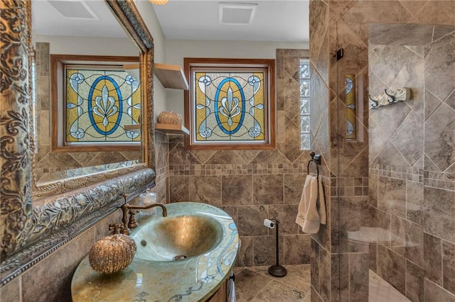 bathroom with tiled shower, vanity, and tile walls