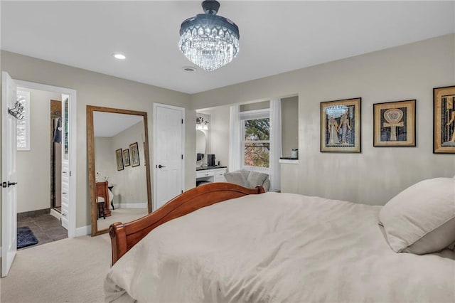 bedroom featuring a notable chandelier, ensuite bathroom, a walk in closet, and light carpet