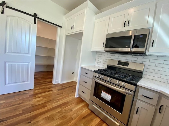 kitchen with light hardwood / wood-style floors, decorative backsplash, a barn door, white cabinetry, and appliances with stainless steel finishes