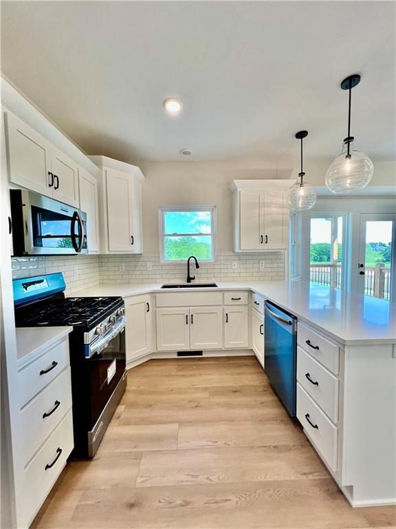 7709 NE 106th Pl, Kansas City, MO 64157 - kitchen featuring appliances with stainless steel finishes, a peninsula, light countertops, white cabinetry, and light wood finished floors