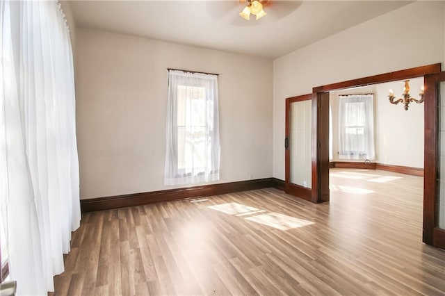 spare room with ceiling fan with notable chandelier, baseboards, and wood finished floors