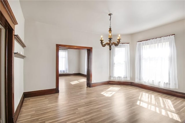 empty room featuring a wealth of natural light, baseboards, a notable chandelier, and light wood-style flooring