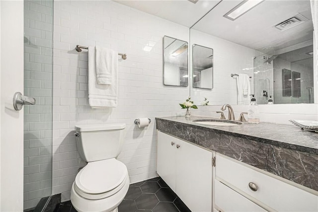 bathroom featuring tile patterned floors, tiled shower, toilet, vanity, and tile walls