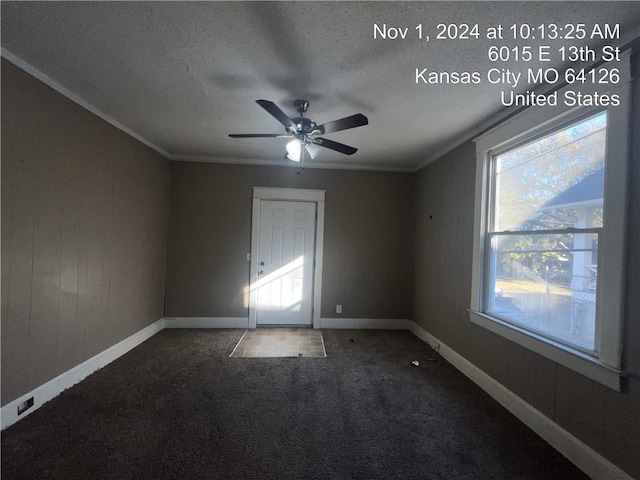 unfurnished room featuring dark colored carpet, ornamental molding, ceiling fan, a textured ceiling, and wooden walls