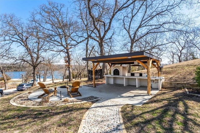 view of yard featuring a patio, an outdoor fire pit, exterior kitchen, a water view, and outdoor dry bar