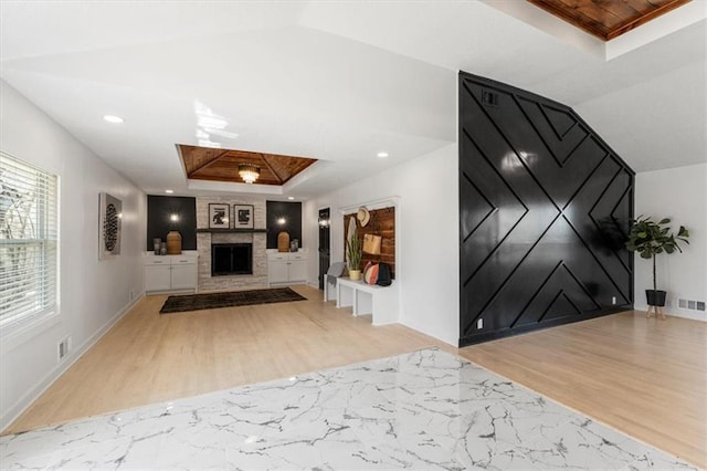 foyer with lofted ceiling, wood finished floors, baseboards, a large fireplace, and a raised ceiling