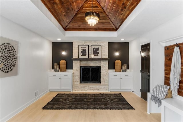 living room featuring a stone fireplace, wooden ceiling, a raised ceiling, and light wood-type flooring