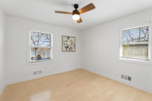 empty room with a wealth of natural light, visible vents, and light wood finished floors