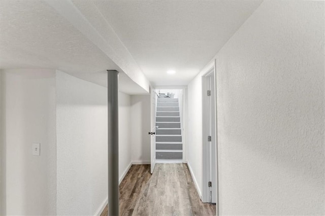 hallway with baseboards, wood finished floors, stairs, a textured wall, and a textured ceiling