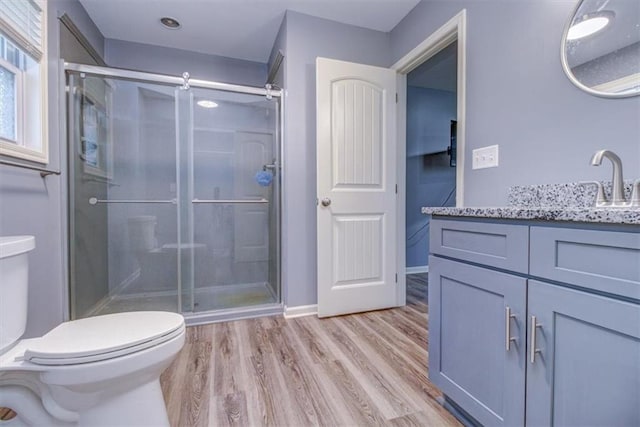 bathroom with wood-type flooring, vanity, toilet, and a shower with shower door