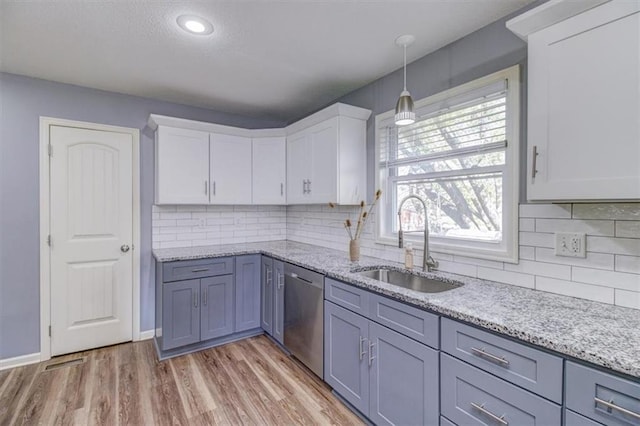 kitchen featuring hanging light fixtures, sink, white cabinets, stainless steel dishwasher, and light hardwood / wood-style flooring