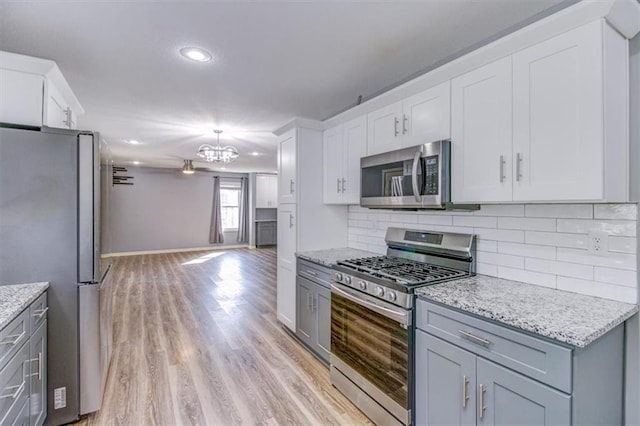 kitchen featuring light hardwood / wood-style floors, an inviting chandelier, decorative backsplash, white cabinetry, and appliances with stainless steel finishes