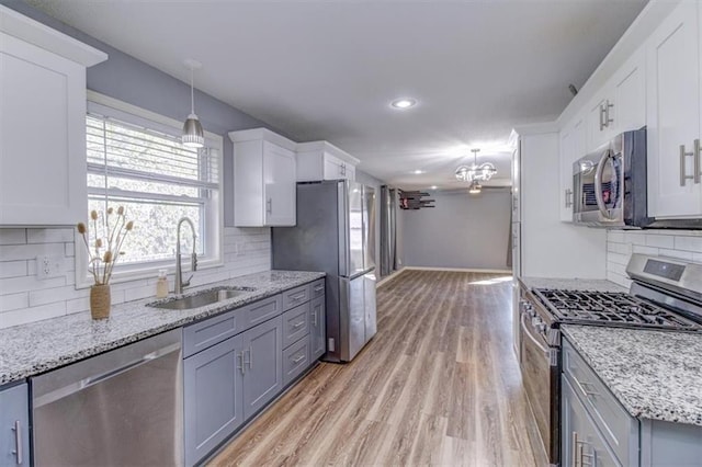 kitchen with appliances with stainless steel finishes, a notable chandelier, sink, light hardwood / wood-style floors, and white cabinets