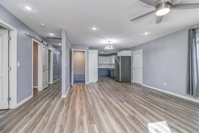 unfurnished living room featuring ceiling fan, a barn door, and light hardwood / wood-style floors