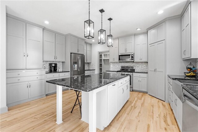 kitchen featuring a breakfast bar area, light hardwood / wood-style floors, decorative light fixtures, a kitchen island, and stainless steel appliances