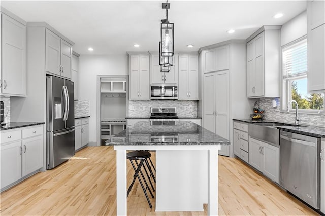 kitchen with appliances with stainless steel finishes, backsplash, pendant lighting, a center island, and light hardwood / wood-style floors