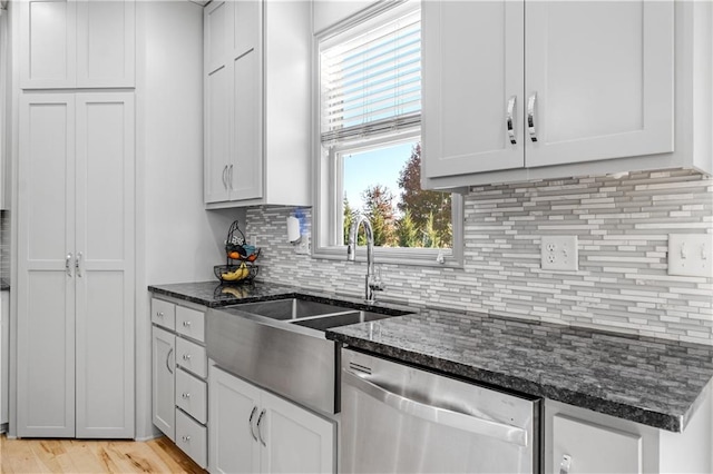 kitchen with white cabinetry, dishwasher, dark stone counters, and light wood-type flooring