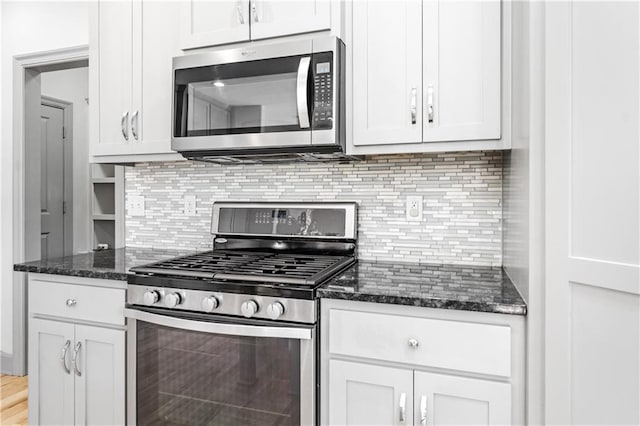 kitchen with white cabinetry, stainless steel appliances, light hardwood / wood-style flooring, dark stone counters, and decorative backsplash